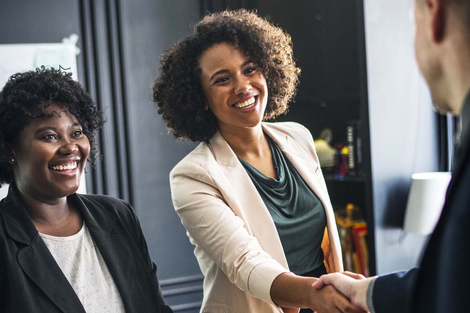 Two women wearing blazers shaking hands with man